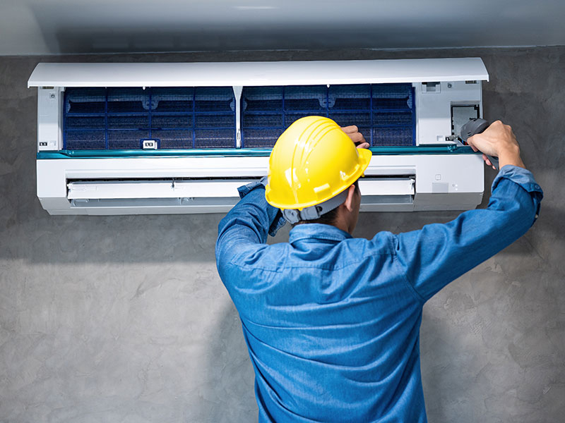 Technician man repairing ,cleaning and maintenance Air conditioner on the wall with screw driver in bedroom or office room.On site home service,Business ,Industrial concept.